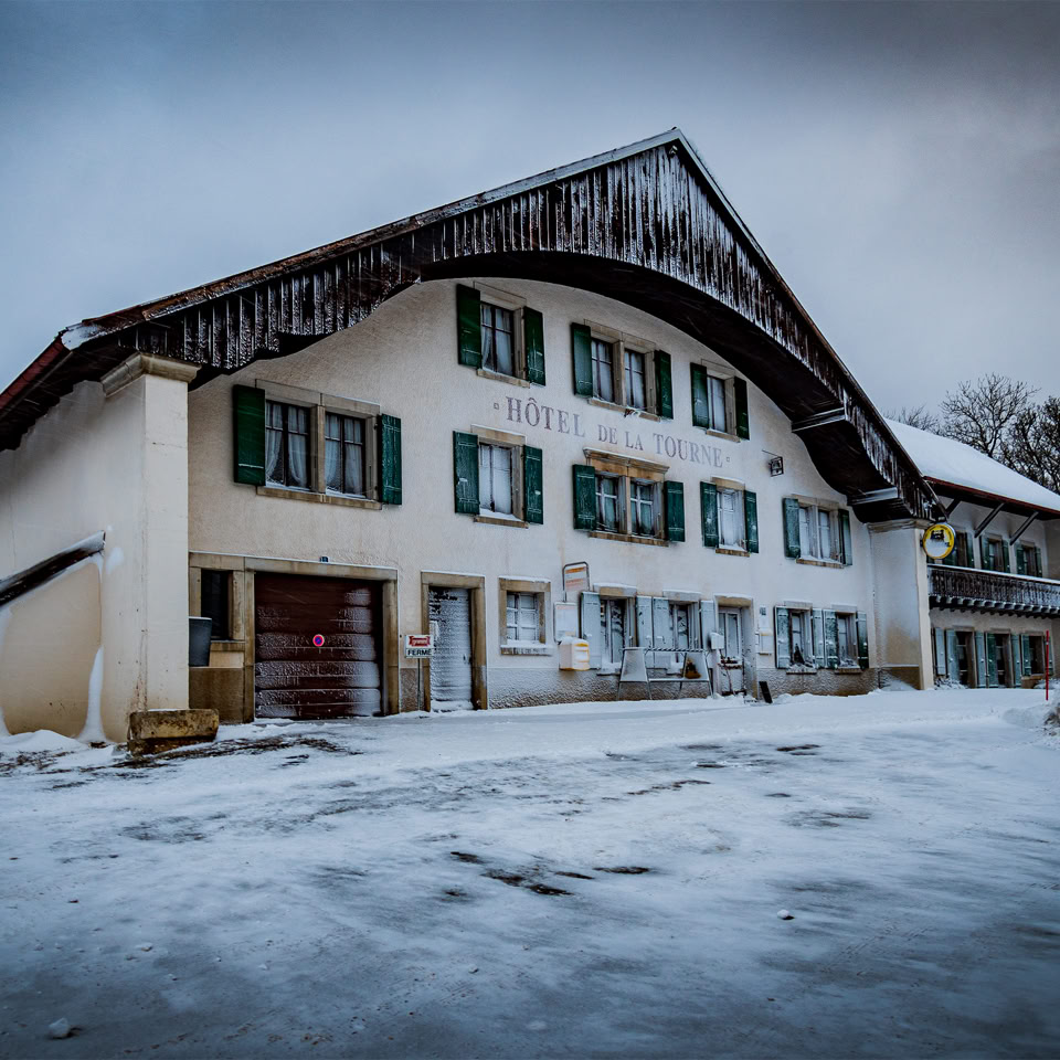 Grande maison enneigée avec des volets verts, sous un ciel nuageux.