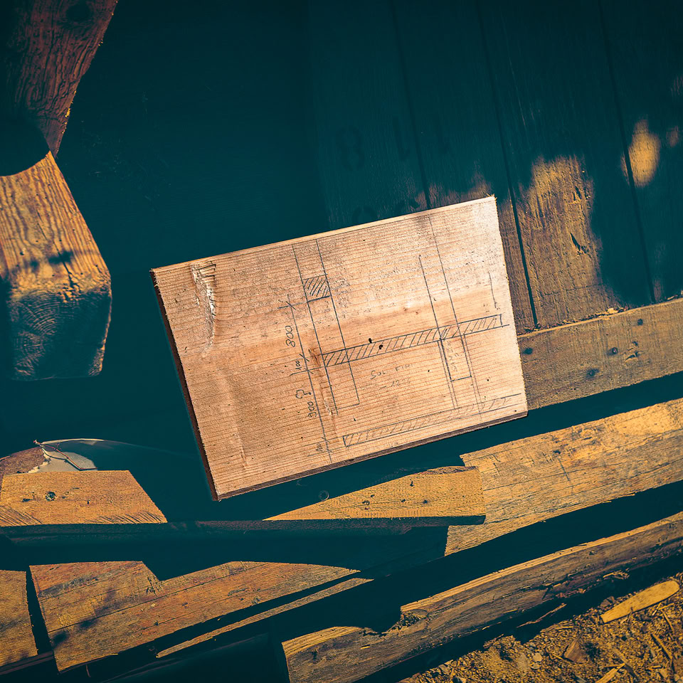Wooden board with a pencil-drawn plan stacked in a dark workshop.