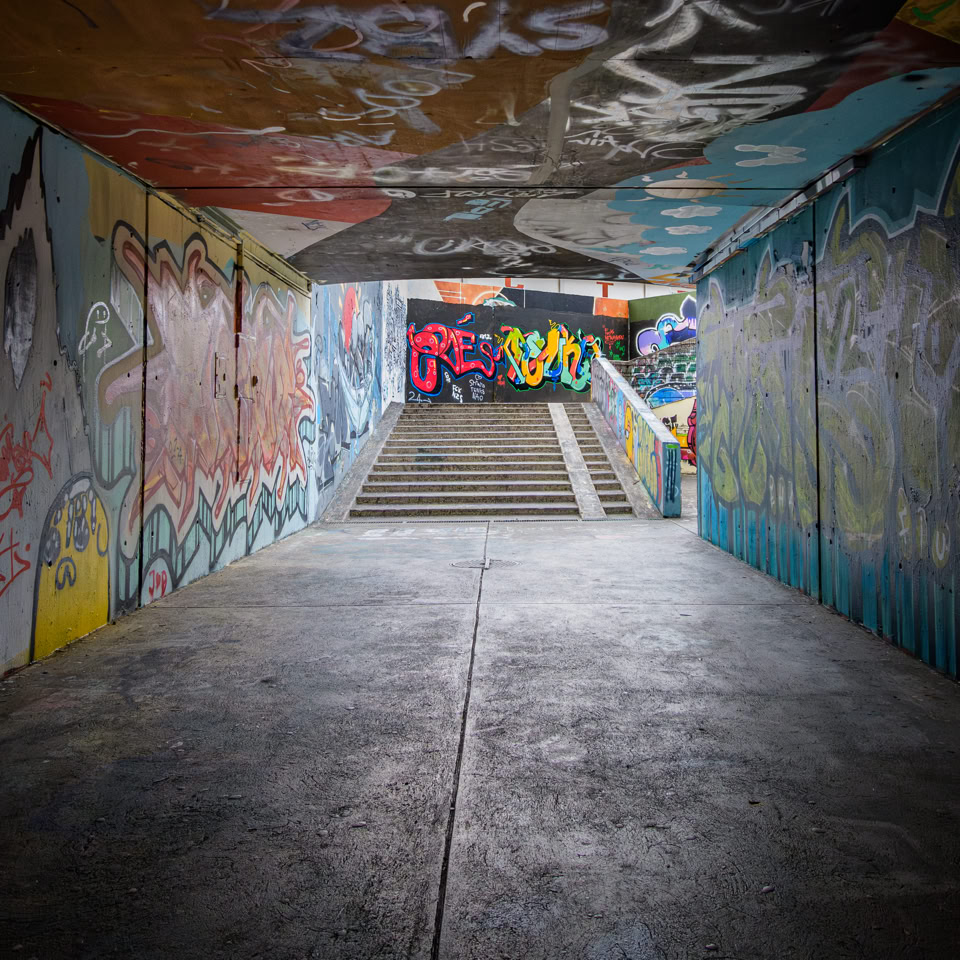 Tunnel avec des murs et un plafond couverts de graffitis colorés, menant à un escalier.