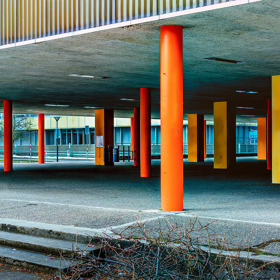 Structure avec des colonnes orange et jaunes sous un toit, avec des escaliers au premier plan.