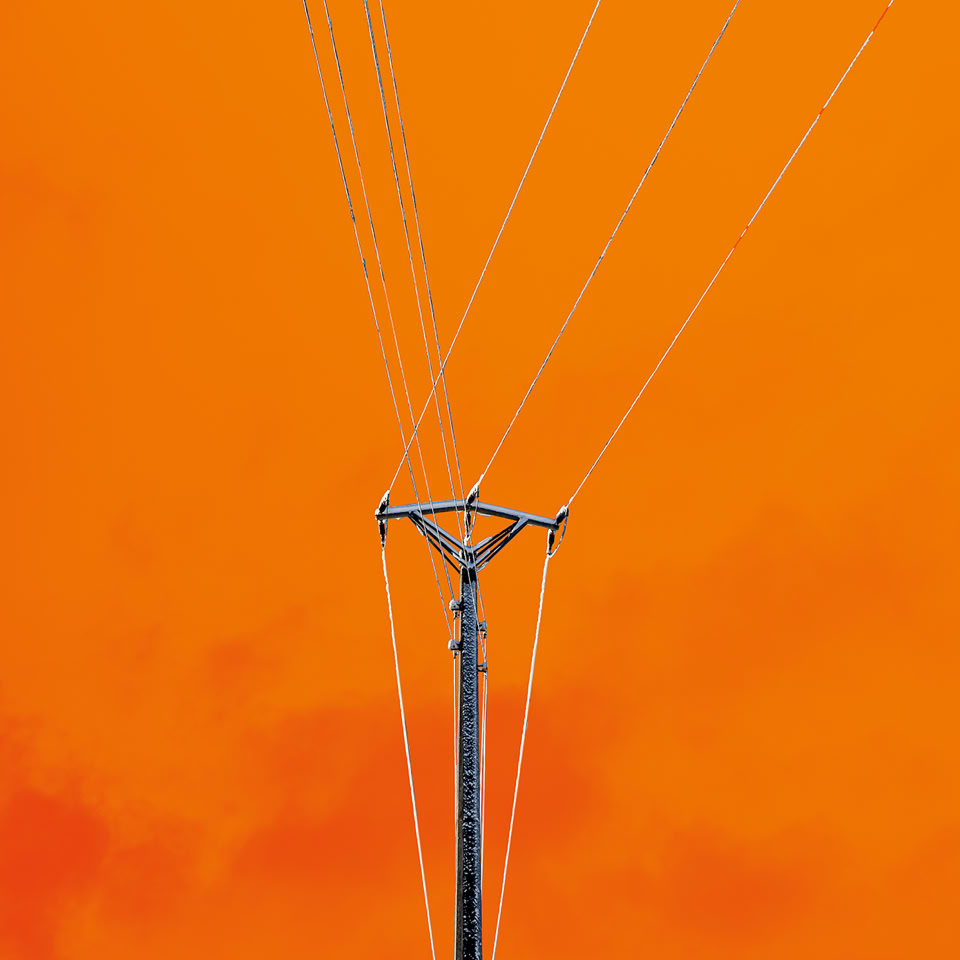 Un poteau électrique avec plusieurs câbles s'étendant vers le haut, sur un fond orange vif.