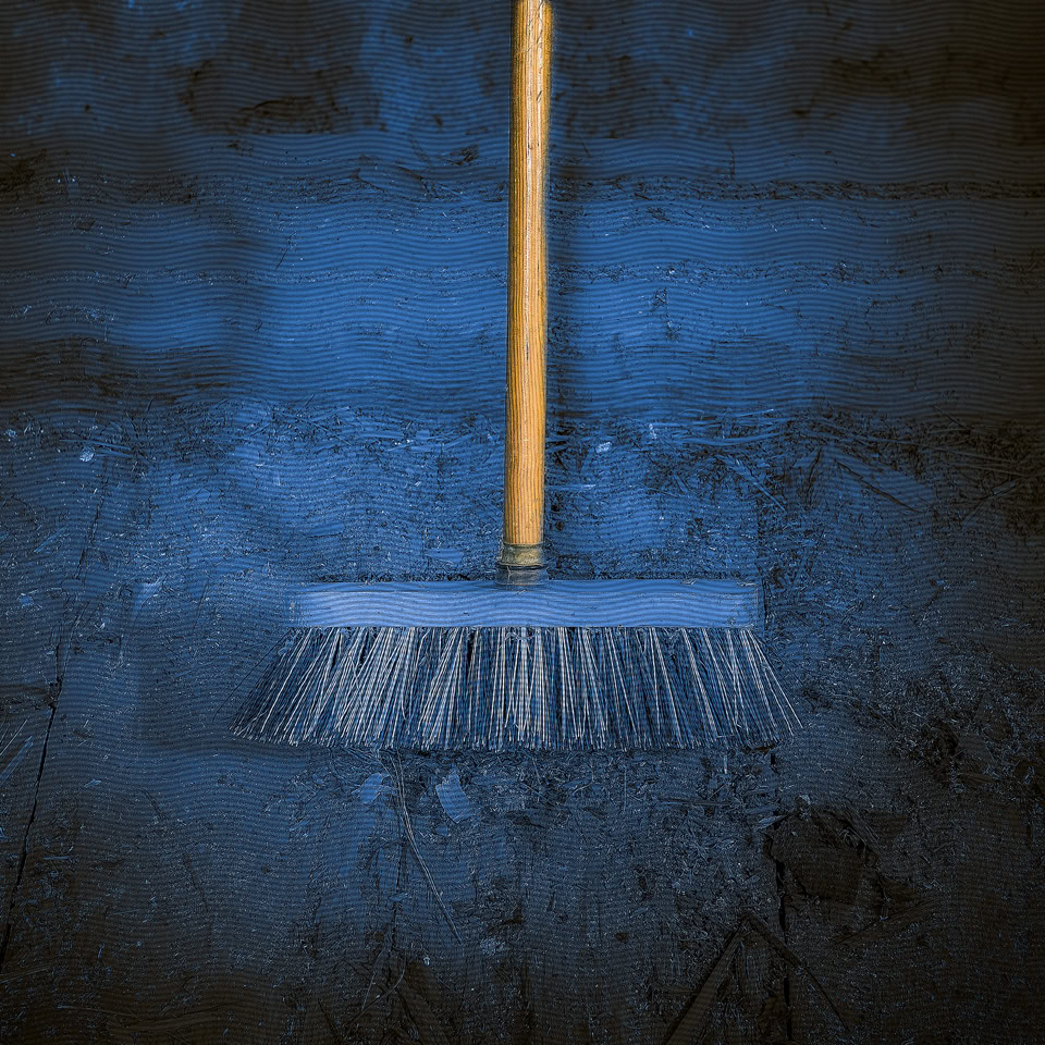 Broom with a wooden handle on a dark blue floor.