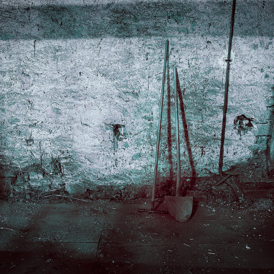 A wooden barn floor, and a shovel and rake leaning against an old lime wall.