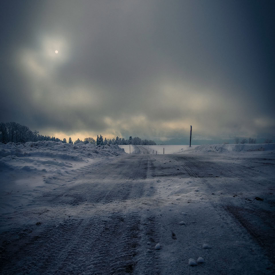 Paysage enneigé avec ciel nuageux et soleil voilé.