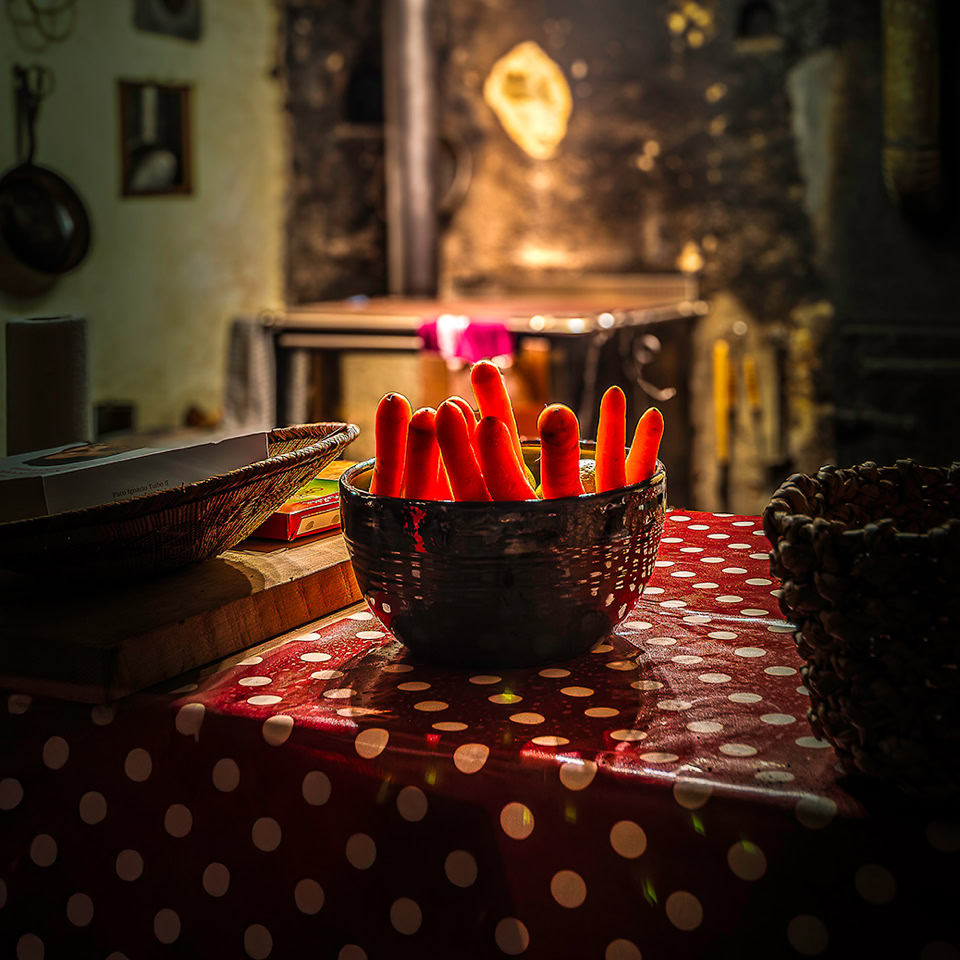 Bowl of carrots on a table with a red and white polka dot tablecloth, blurred interior in the background.