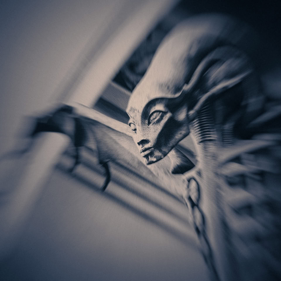 A blurred, monochromatic image of a skeletal figure with an elongated head and visible ribs, reaching out with one arm.