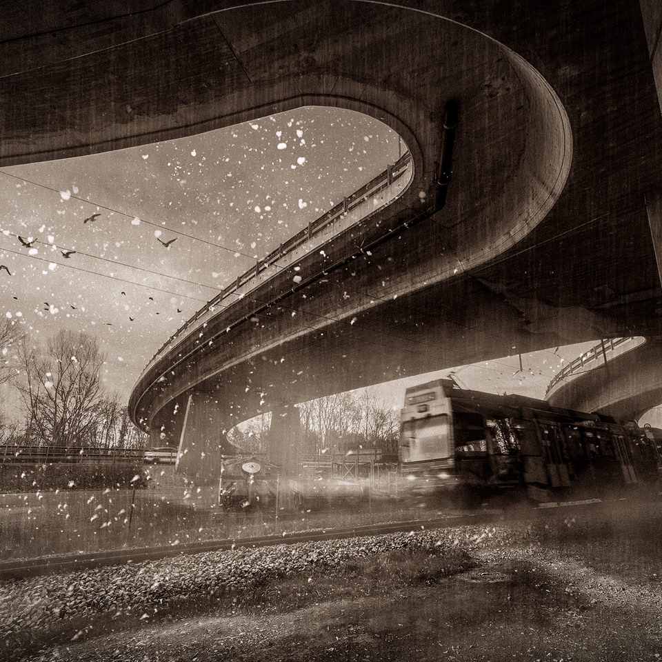 A sepia-toned image of a curved highway overpass with a train passing underneath, surrounded by rain and wet surfaces.