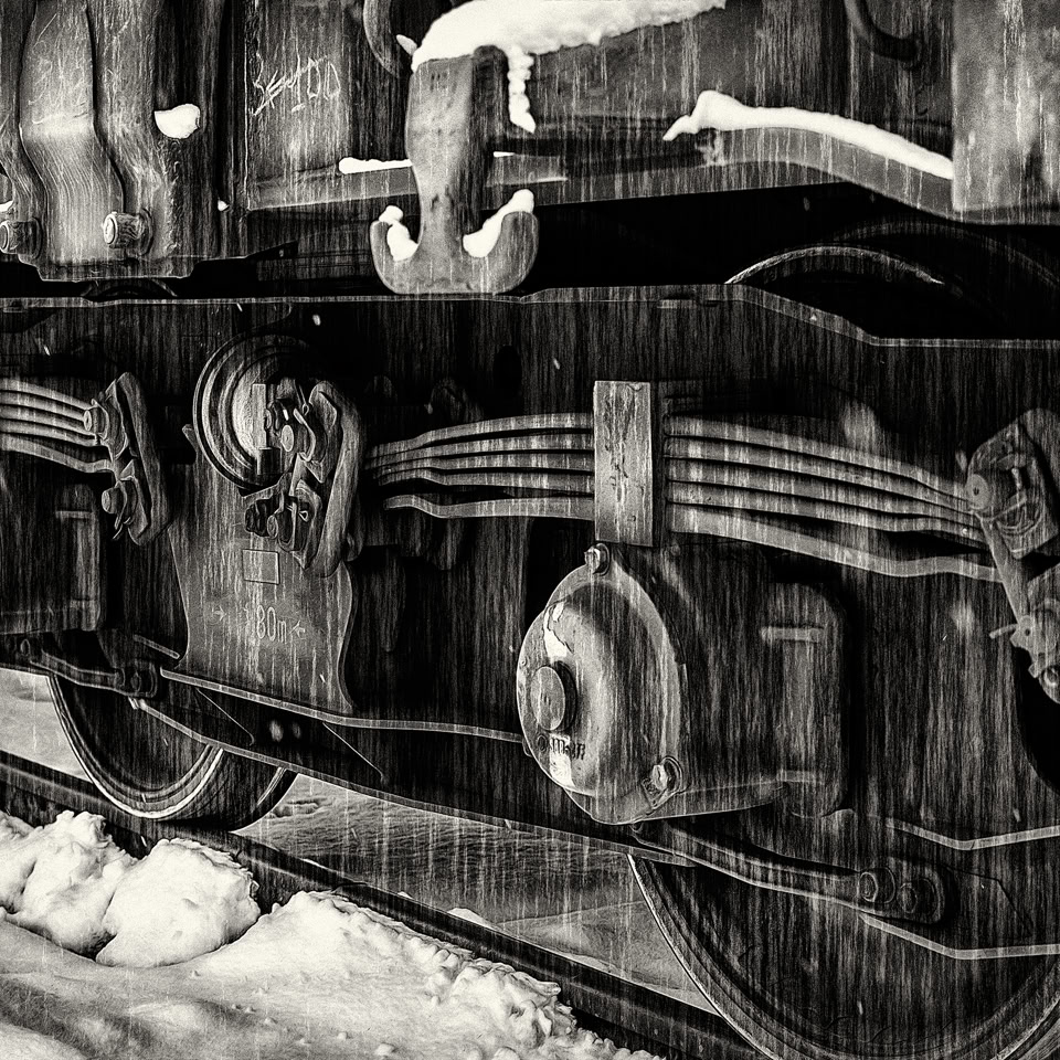 Close-up of a train wheel and suspension system on a snowy track.